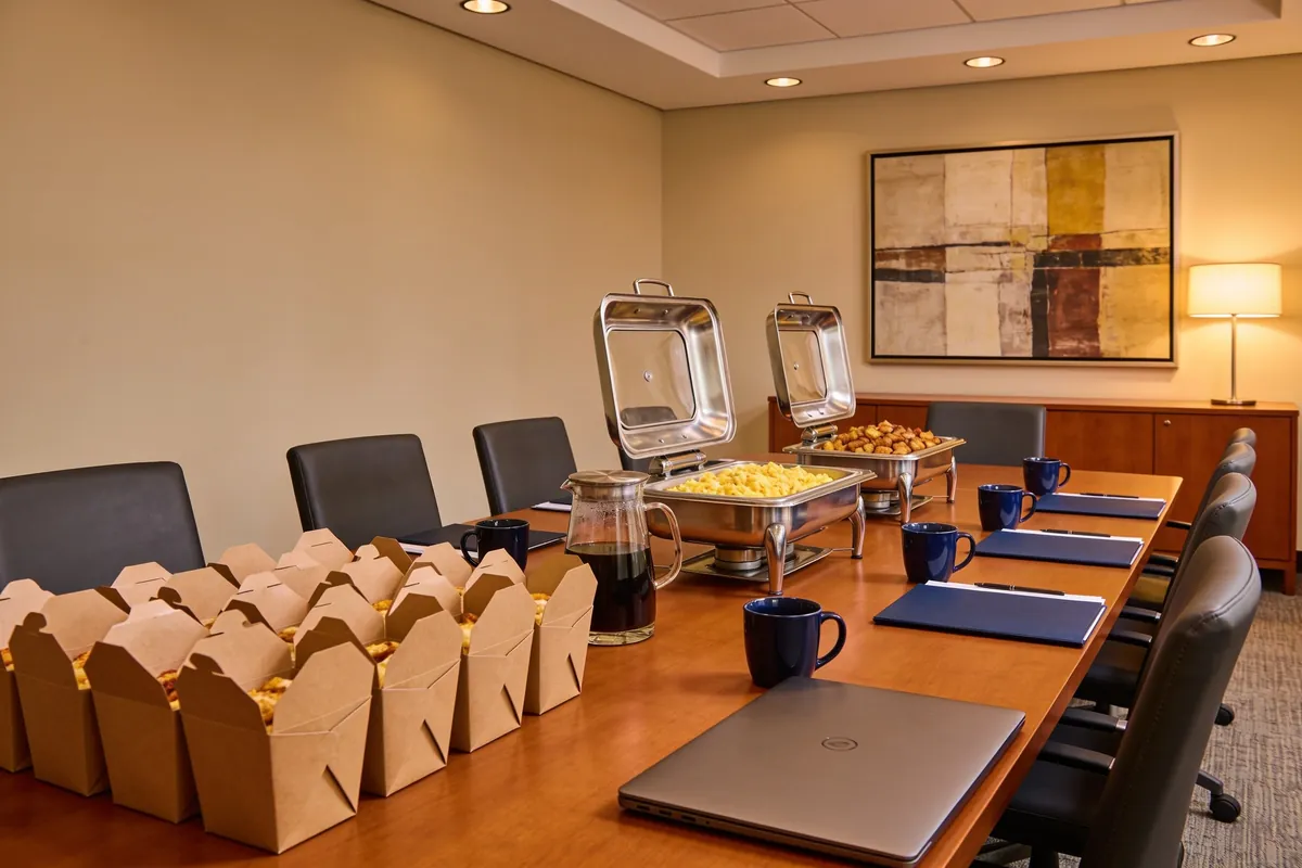 U.S. Egg catering setup in a government conference room โ kraft breakfast boxes, chafing trays, and navy mugs arranged on a long boardroom table